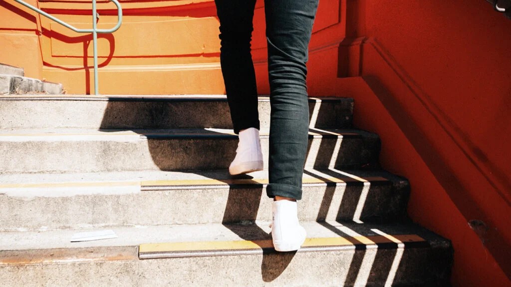 A person wearing white sneakers and black pants walks up a flight of stairs